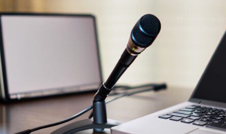 A microphone on a desk with a laptop and a pen. The image has a professional and inviting look.